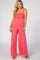 woman wearing a coral pink maternity jumpsuit with smocked bodice and wide-legged pants, model poses smiling