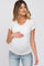 woman wearing a white short sleeve maternity top and holding her baby bump while smiling