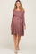 woman wearing a mauve long sleeve maternity dress with a tie waist and flared skirt, showcasing her baby bump