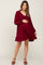 pregnant woman wearing a burgundy long sleeve maternity dress with ruffle hem and v-neckline