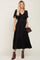 Woman wearing a black smocked midi dress with flutter sleeves, brown boots, and a crossbody bag