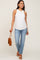 woman wearing a white ribbed maternity tank top and blue jeans, holding a brown purse