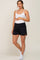 woman wearing a white tank top and black maternity shorts, holding her baby bump