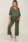 woman wearing an olive green maternity top and matching pants, showing her baby bump while standing on a neutral background