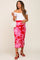 woman wearing a white off-the-shoulder top and a red floral maternity skirt, holding a small white handbag
