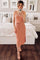 woman wearing a coral ribbed midi dress with a tie waist and side slit, standing in a stylish bedroom setting