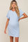 woman wearing a light blue maternity dress with short sleeves and a chest pocket, showing her baby bump