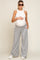 woman wearing a white ribbed maternity tank top and gray wide-leg sweatpants, holding her baby bump