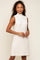 Woman wearing a white sleeveless cable knit sweater dress with a mock neck and gold jewelry