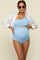 woman wearing a light blue maternity swimsuit with a one-shoulder design and cut-out detail, styled with a white shirt and sunglasses.