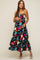 Smiling pregnant woman in a black floral tiered maternity maxi dress with spaghetti straps and white heels
