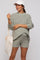 woman wearing a light green oversized knit maternity sweater and matching shorts, holding a tote bag and wearing a cap