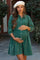 woman wearing a green corduroy maternity dress with button details and a beret, holding her baby bump