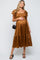 woman wearing a rust brown maternity dress with ruffled sleeves and a tiered skirt, holding her baby bump