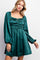 woman wearing a green satin long sleeve dress with ruched detailing and a square neckline
