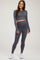 woman wearing a gray long sleeve maternity crop top and matching maternity leggings, smiling and standing in a relaxed pose