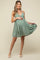 woman wearing a sage green maternity dress with spaghetti straps and a flowing skirt, holding her baby bump