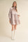 woman wearing a light mauve long sleeve mini dress with ruffle details and high neck, paired with white knee-high boots