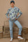 woman wearing a floral patterned light blue maternity sweater and light blue jeans, posing with a baby bump visible