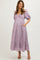 woman wearing a lavender maternity dress with puff sleeves and pockets, showing her baby bump