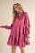 woman wearing a pink tiered mini dress with long sleeves and smocked detailing on the neckline and cuffs