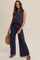 woman wearing a navy sleeveless top and wide-leg pants with a straw hat and sandals