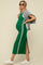 woman wearing a green maternity maxi dress with side stripes and a high slit, holding a gray sweater and showing her baby bump