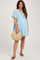 woman wearing a light blue maternity dress with a tiered skirt and holding a straw crossbody bag