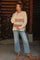 woman wearing a neutral colored knitted maternity sweater with stripes and blue wide-leg maternity jeans, holding her baby bump