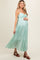 woman wearing a mint green maternity maxi dress with spaghetti straps and a flowing tiered skirt, showcasing her baby bump