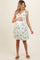woman wearing a white floral maternity dress with tie straps and holding her baby bump