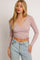 woman wearing a light pink long sleeve crop top with adjustable side ties and v-neckline, paired with high-waisted jeans