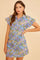 woman wearing a short sleeve floral button-up dress in blue, purple, and green with ruffled sleeves