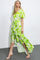 woman wearing a bright green floral maxi dress with puff sleeves and a ruffled hem, standing in profile