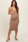 woman wearing a tan ribbed maternity dress with a deep v-neck and buttons, holding her baby bump
