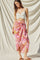 woman wearing a white knotted crop top and a pink floral wrap skirt with a high-low hem