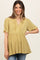 woman wearing a mustard yellow maternity top with a v-neck and ruffled hem, smiling at the camera