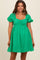 woman wearing a green short puff sleeve maternity dress with a square neckline and gathered bodice