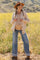 woman wearing a cream cardigan over a striped maternity top and flared jeans, displaying her baby bump in a field