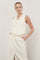 woman wearing a cream sleeveless tailored vest with double buttons and pockets, paired with a matching skirt