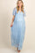woman wearing a light blue maternity maxi dress with floral embroidery and a visible baby bump, standing in front of colorful balloons