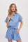 Woman wearing a light blue short sleeve button-up romper with a tie waist and pockets against a white background