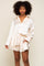 Woman wearing cream satin button-down shirt and matching shorts lounge set with gold chain necklace