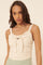 woman wearing a cream-colored sleeveless top with a front tie and ruched detailing