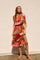 woman wearing a vibrant floral midi dress with a side slit and short sleeves, posed against a white wall