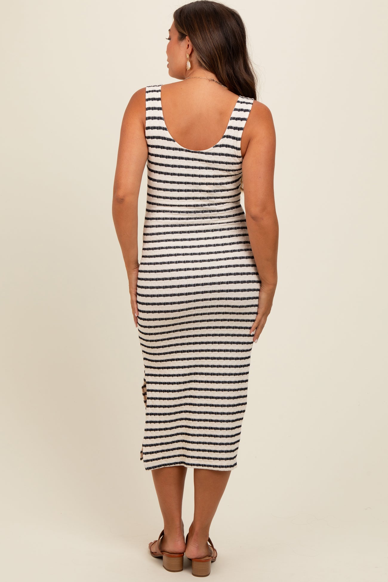 woman wearing a striped maternity dress with a sleeveless design and side button details, showing a baby bump