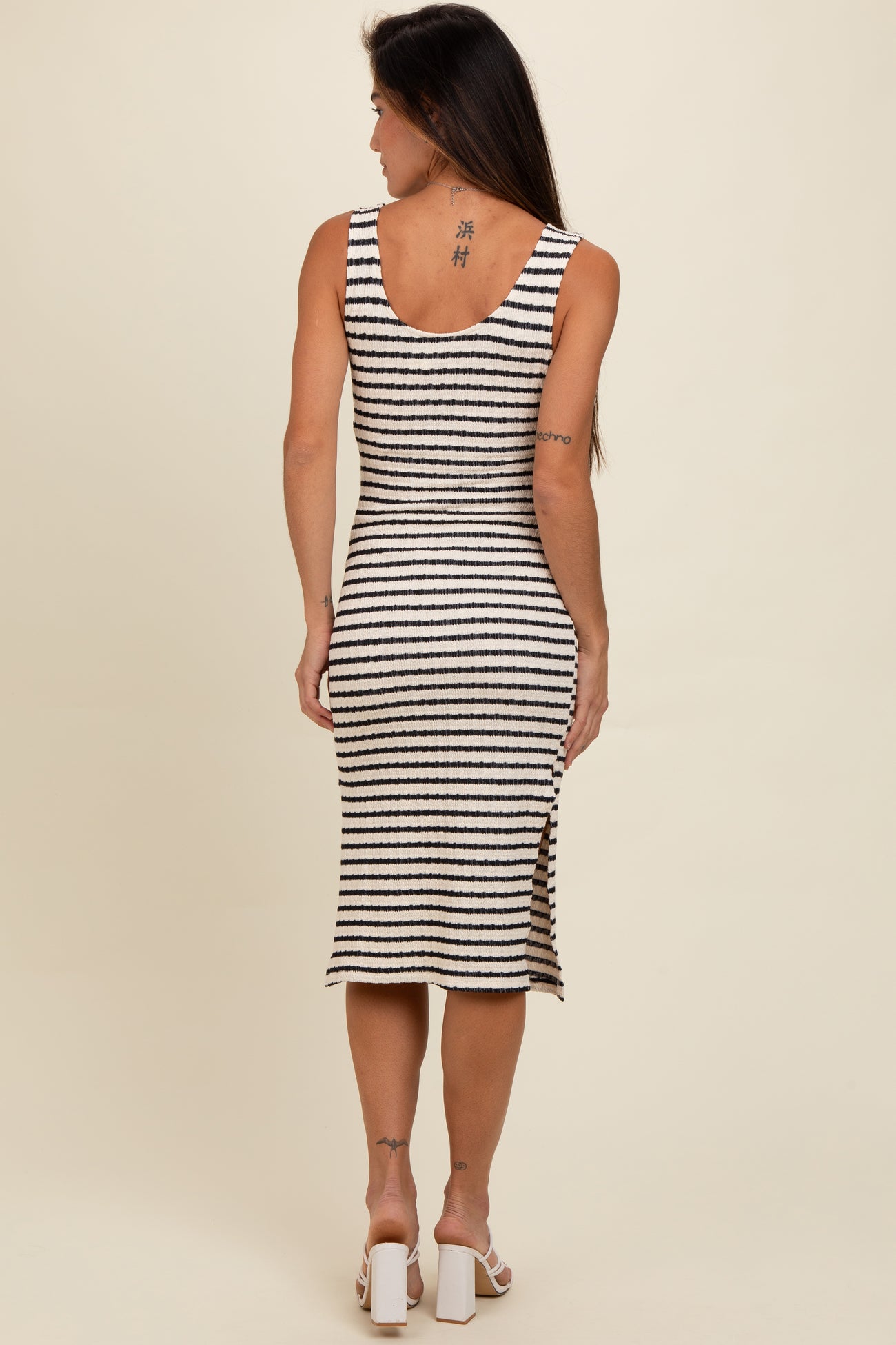 woman wearing a black and white striped sleeveless midi dress with side slit, seen from the back