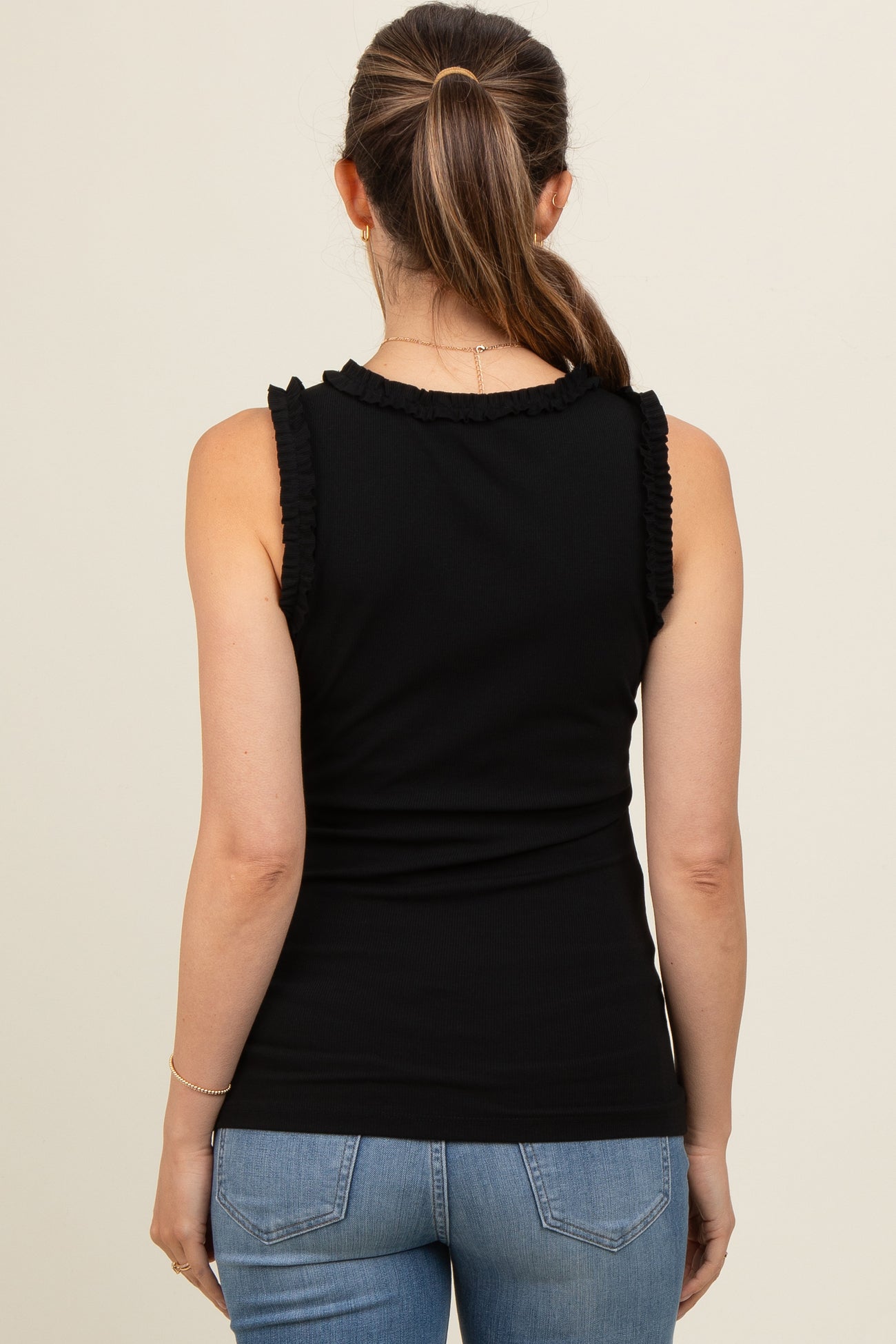 woman wearing a black maternity tank top with ruffle details and light blue jeans, showing her back