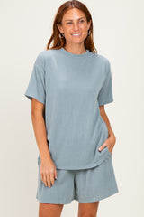 woman wearing a light blue ribbed short sleeve top and matching shorts, smiling with hands in pockets