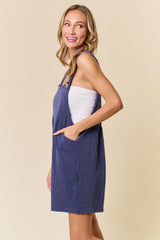 woman wearing a navy blue striped overall dress with pockets and a white tank top underneath